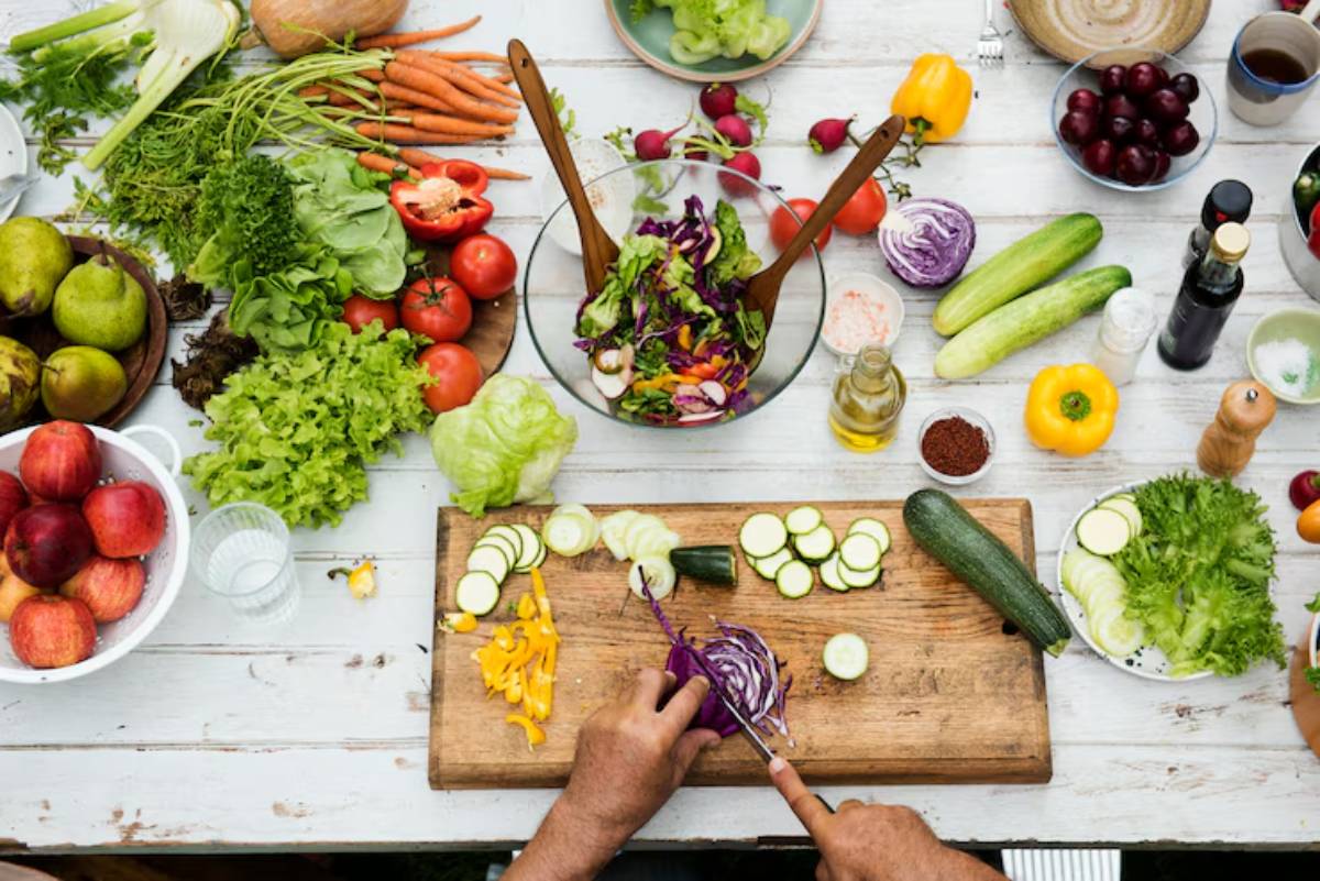 A top-down view of a vibrant kitchen scene with fresh vegetables being chopped on a wooden cutting board. 