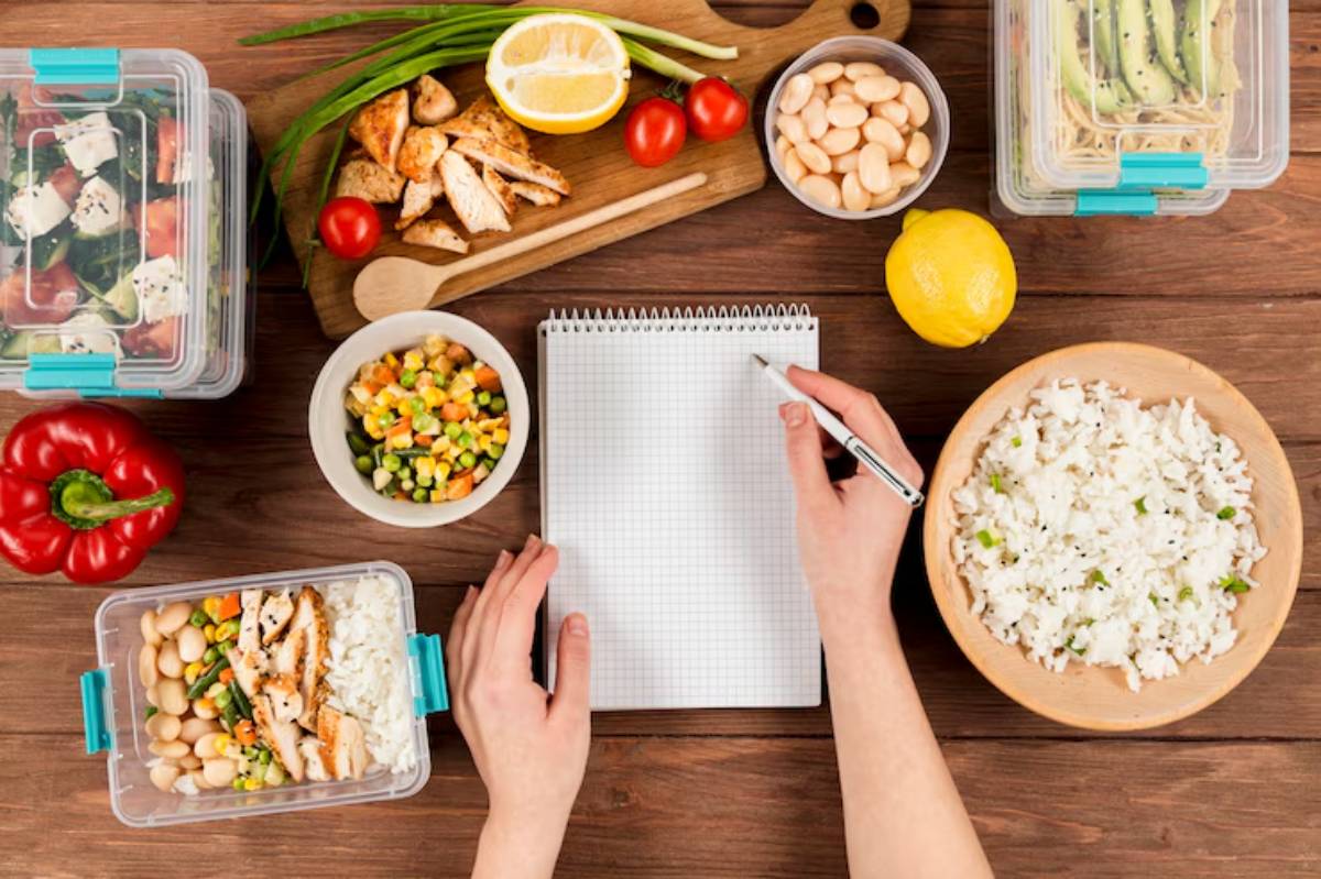 A overhead view of meal prep featuring containers of salad, chicken, rice, vegetables, and a notepad with a pen.