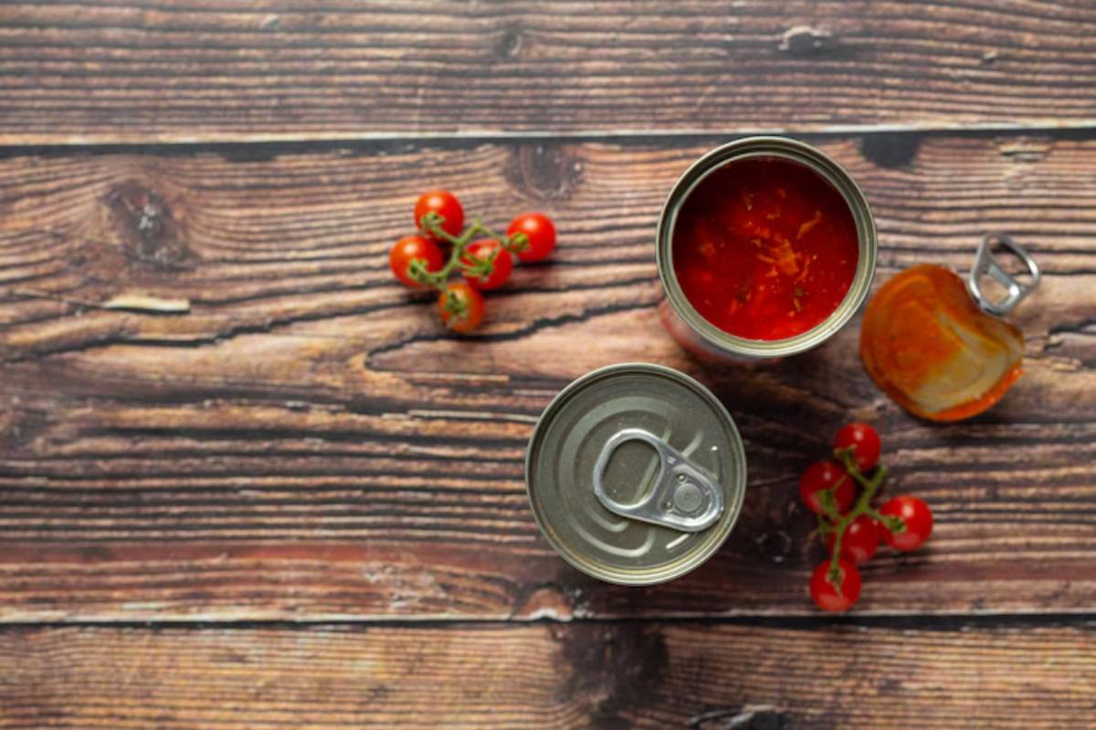 A top-down view of an open can of tomato sauce beside fresh cherry tomatoes on a wooden surface.