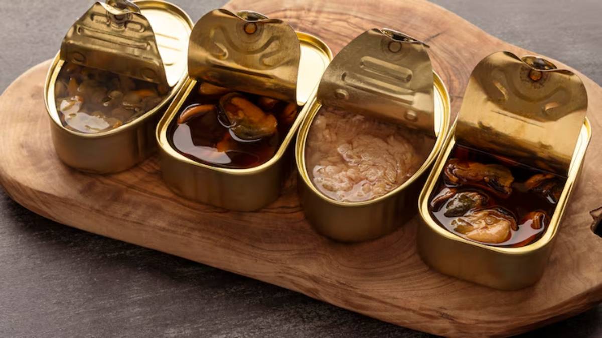 Three opened golden cans of seafood, showcasing mussels and fish in glossy sauces, arranged on a wooden serving board.