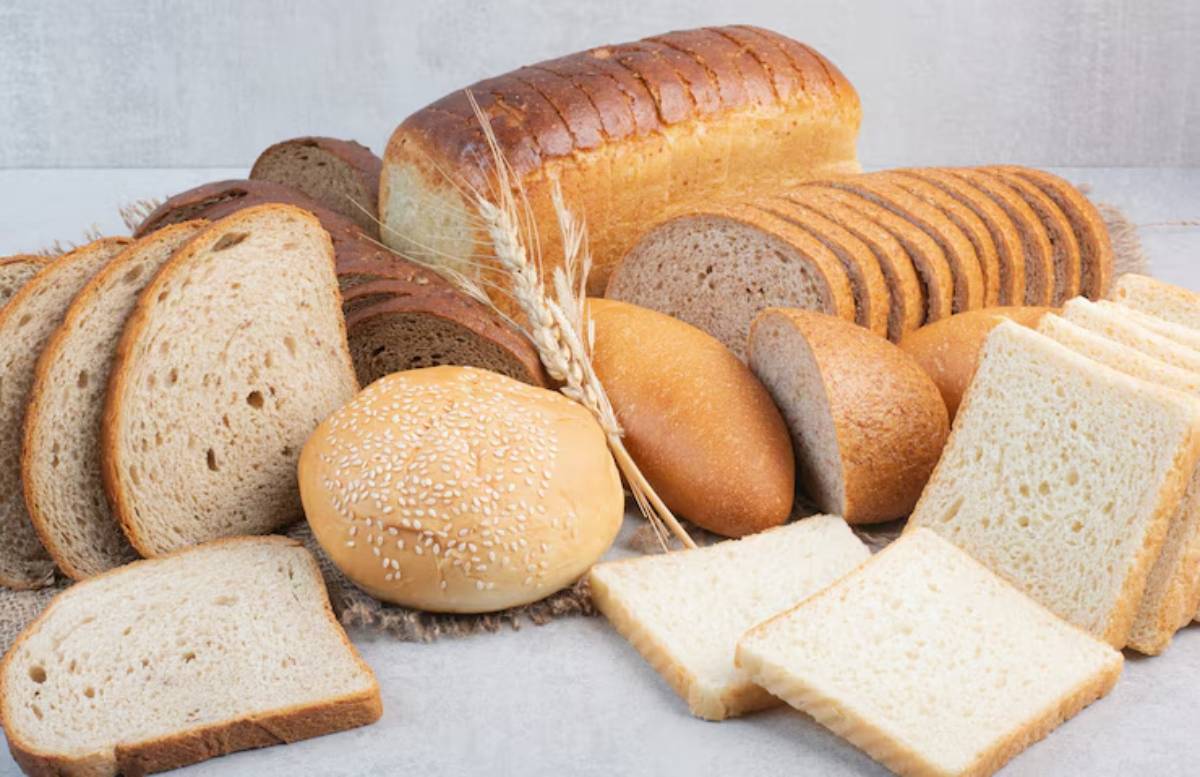 An assortment of various types of bread, including sliced loaves, rolls, and a sesame bun, arranged attractively on a surface.