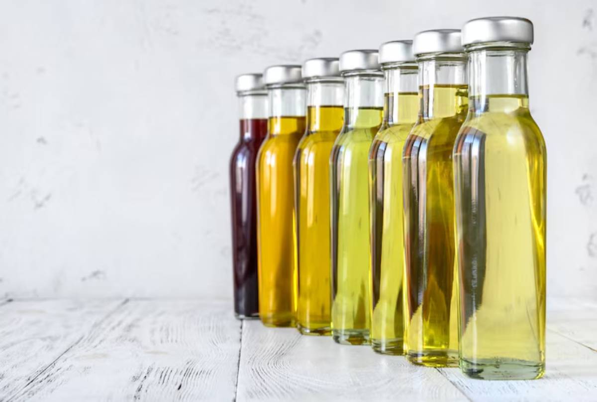 A row of eight glass bottles filled with various colored oils, ranging from dark to light, against a white textured background.