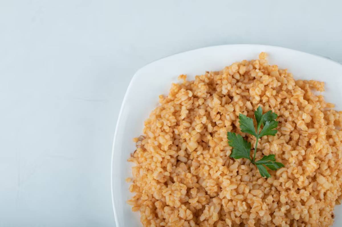 A serving of fluffy, golden-brown bulgur wheat garnished with a sprig of fresh parsley on a white plate.