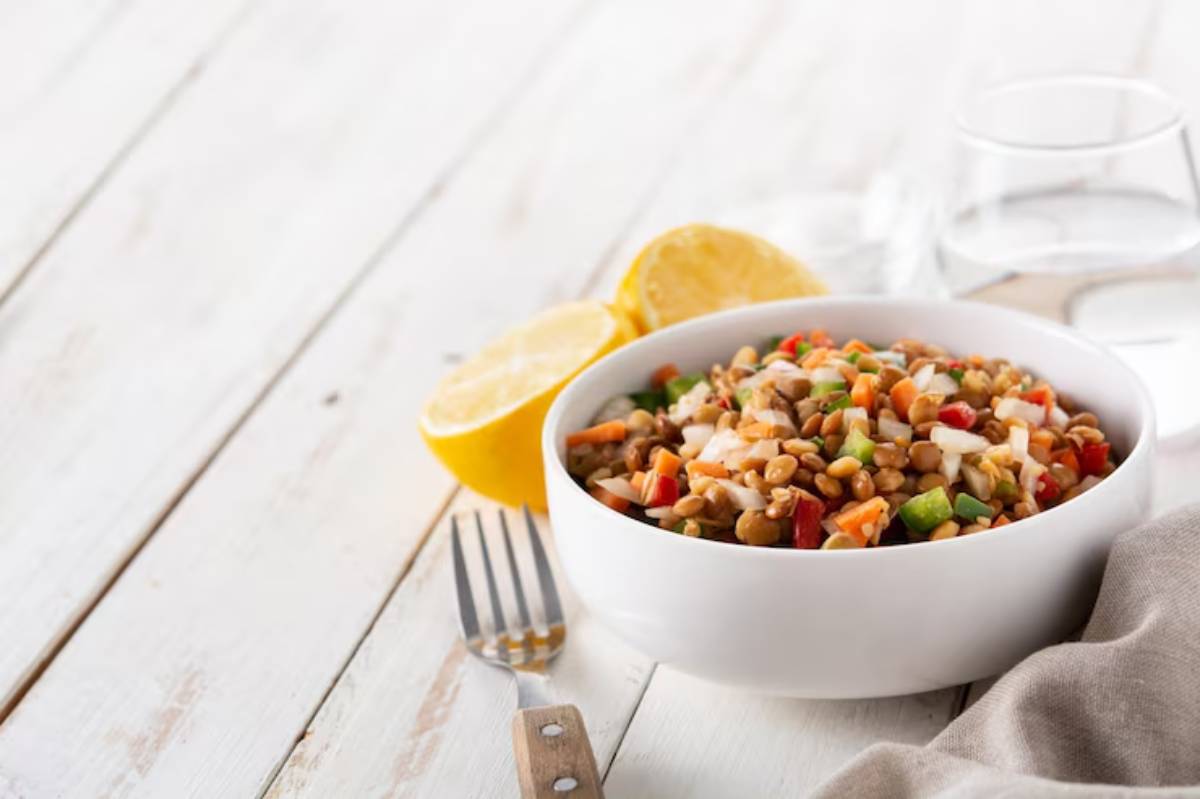 A white bowl filled with a colorful grain and vegetable salad, garnished with lemon halves, on a rustic wooden table.