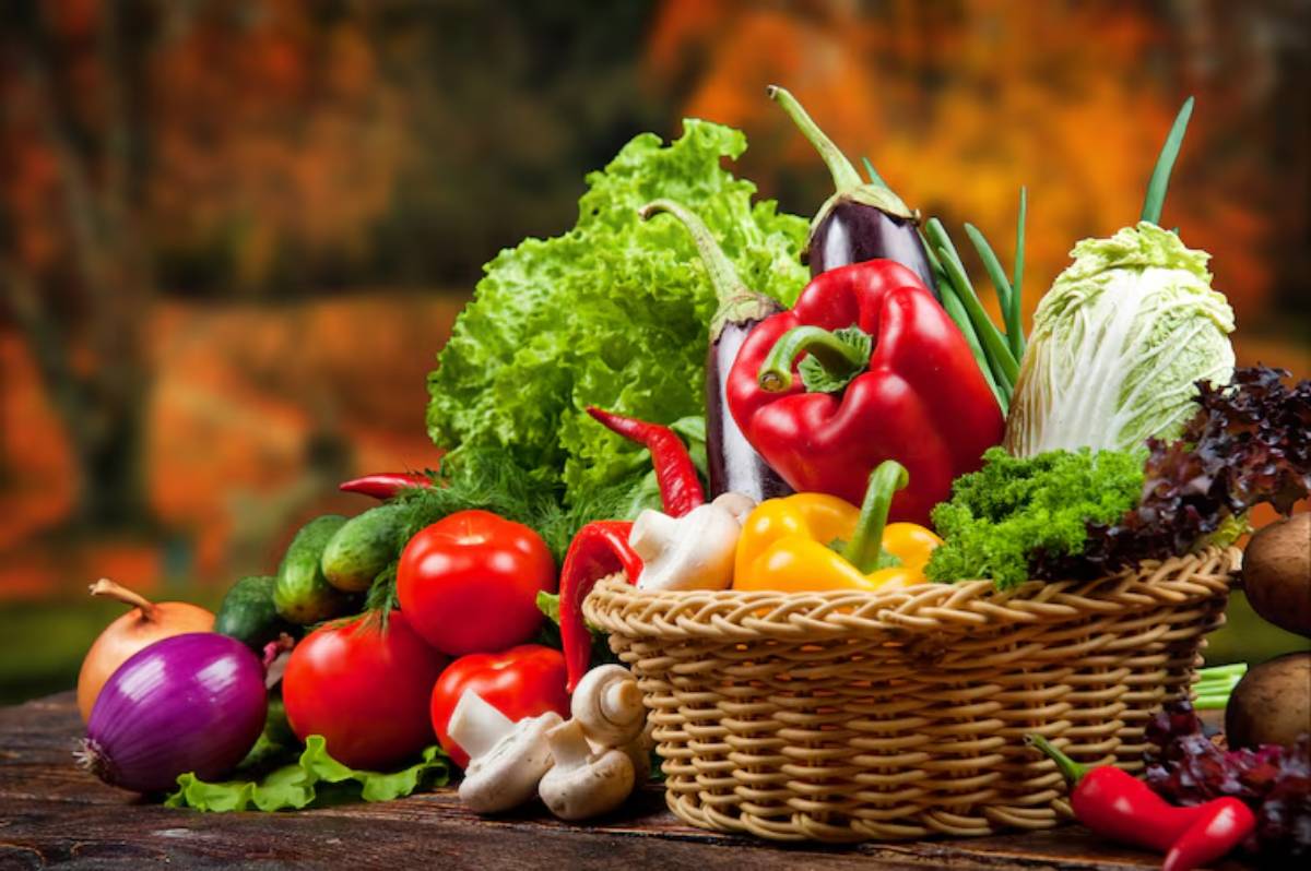 A bountiful assortment of fresh vegetables including peppers, lettuce, tomatoes, mushrooms, and cucumbers in a woven basket.