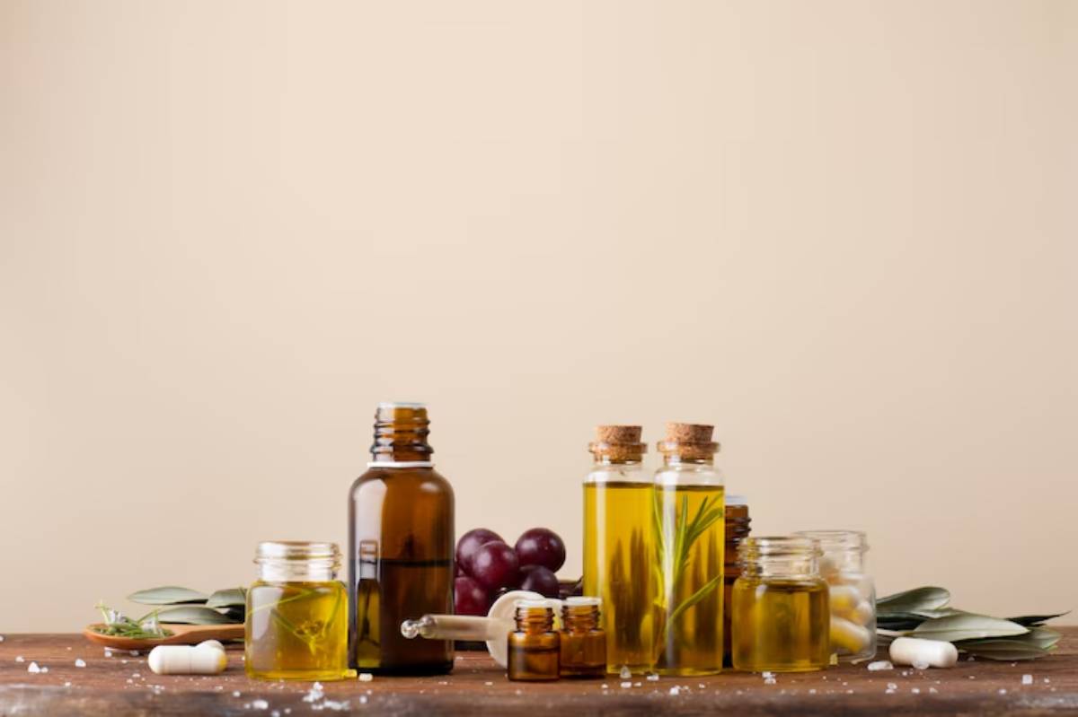 A rustic wooden table holds various glass jars and bottles of oils, herbs, and capsules against a light beige background.