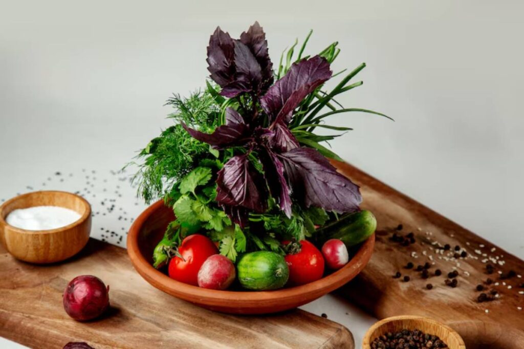 A wooden bowl filled with fresh herbs, tomatoes, cucumbers, and radishes, accompanied by a small bowl of yogurt and spices.