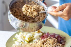 A person scoops cooked rice from a pot onto a plate, accompanied by sliced apples and red onions.