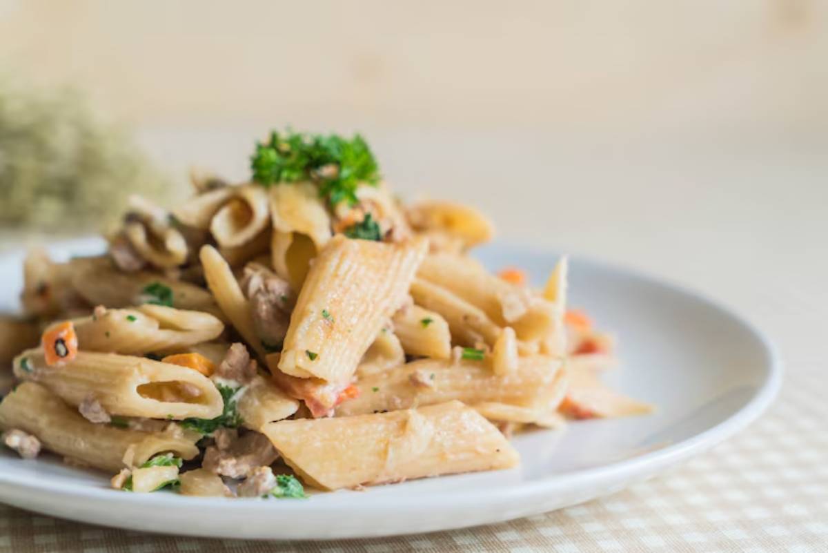 A plate of creamy penne pasta with chopped herbs, diced vegetables, and minced meat, garnished with parsley.