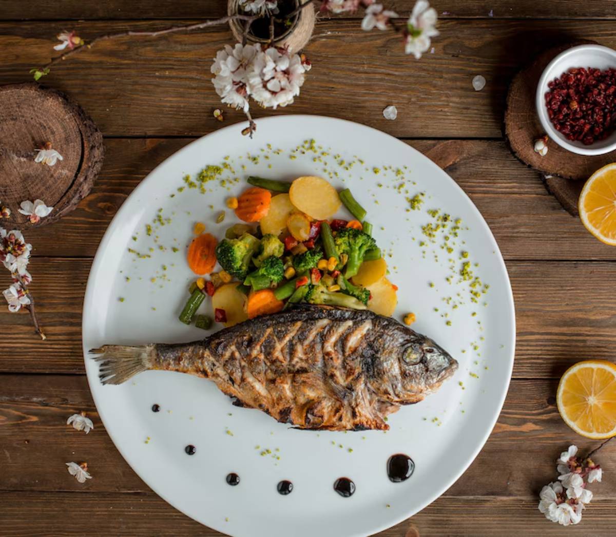 Grilled whole fish served on a white plate with a medley of colorful vegetables, garnished with herbs and a drizzle of sauce.