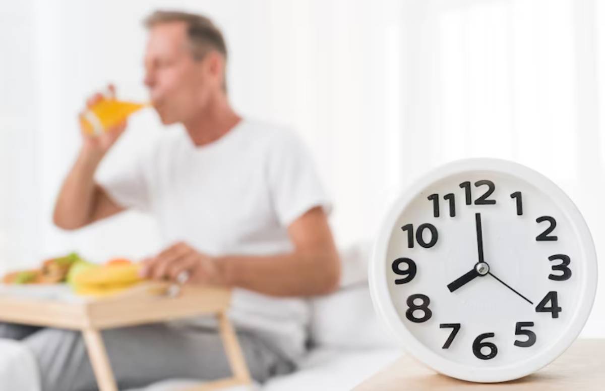 A man enjoys breakfast on a tray, sipping a drink, with a large white clock displaying 10:10 in the foreground.