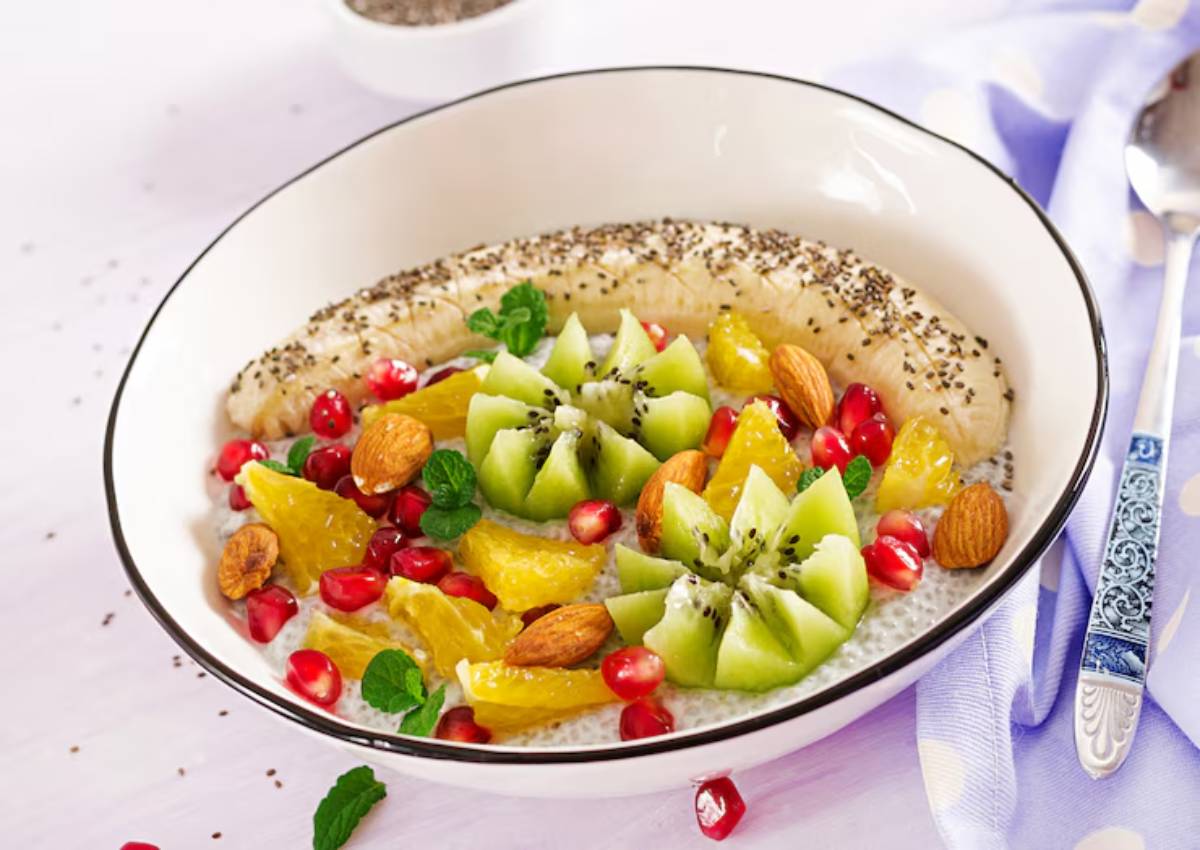 A bowl of chia seed pudding topped with banana, kiwi, orange segments, pomegranate seeds, almonds, and mint leaves.