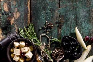 An array of olives, herbs, spices, and cheese cubes on a rustic wooden table, showcasing vibrant colors and textures.