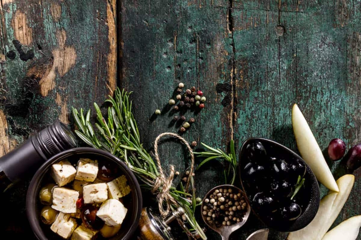 An array of olives, herbs, spices, and cheese cubes on a rustic wooden table, showcasing vibrant colors and textures.