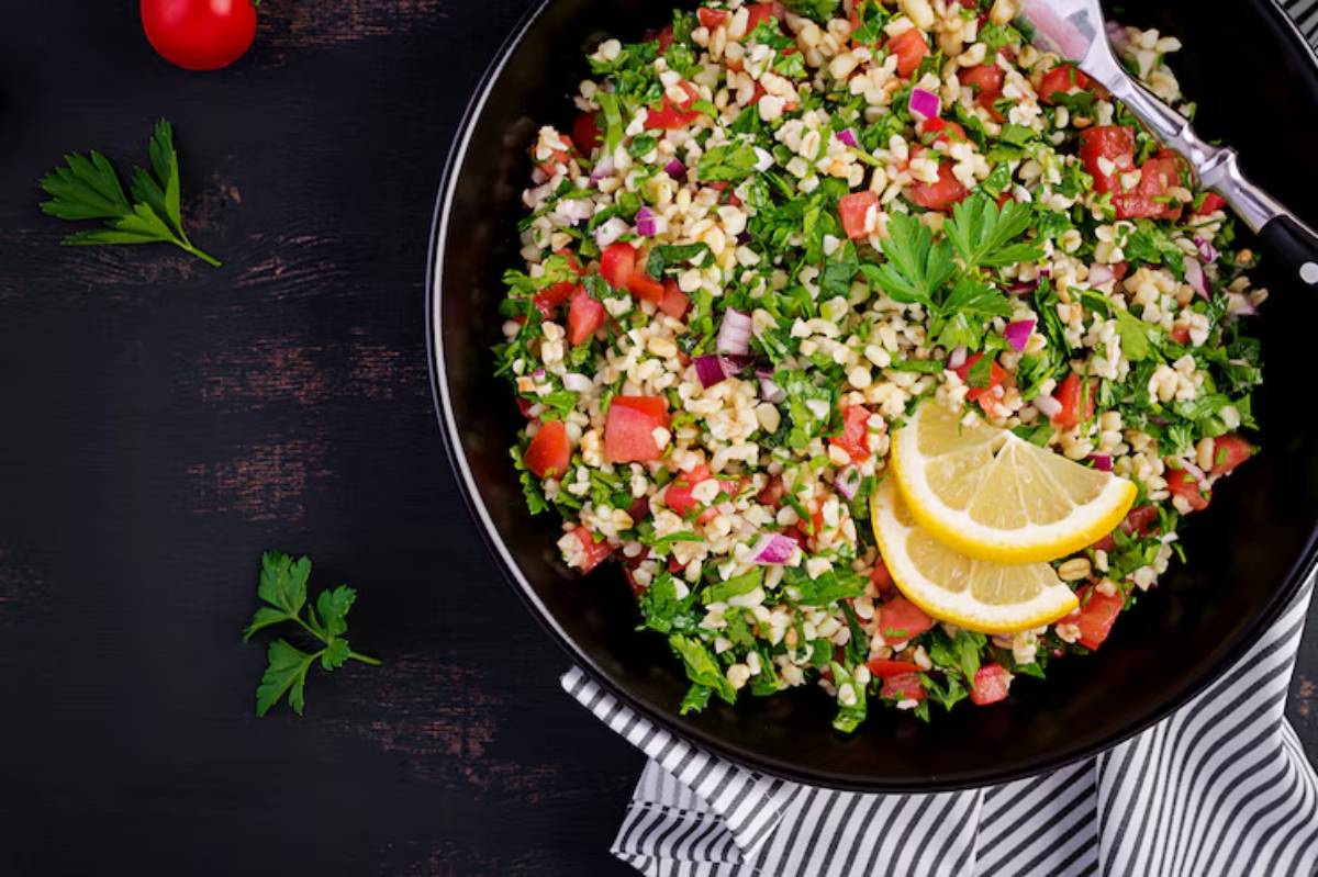A black bowl filled with tabbouleh salad, featuring parsley, tomatoes, and bulgur, garnished with lemon slices, on a striped napkin.