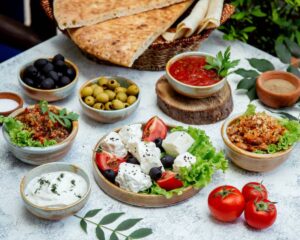 A vibrant spread of Mediterranean dishes including olives, feta, tomatoes, dips, and flatbread, garnished with fresh herbs.