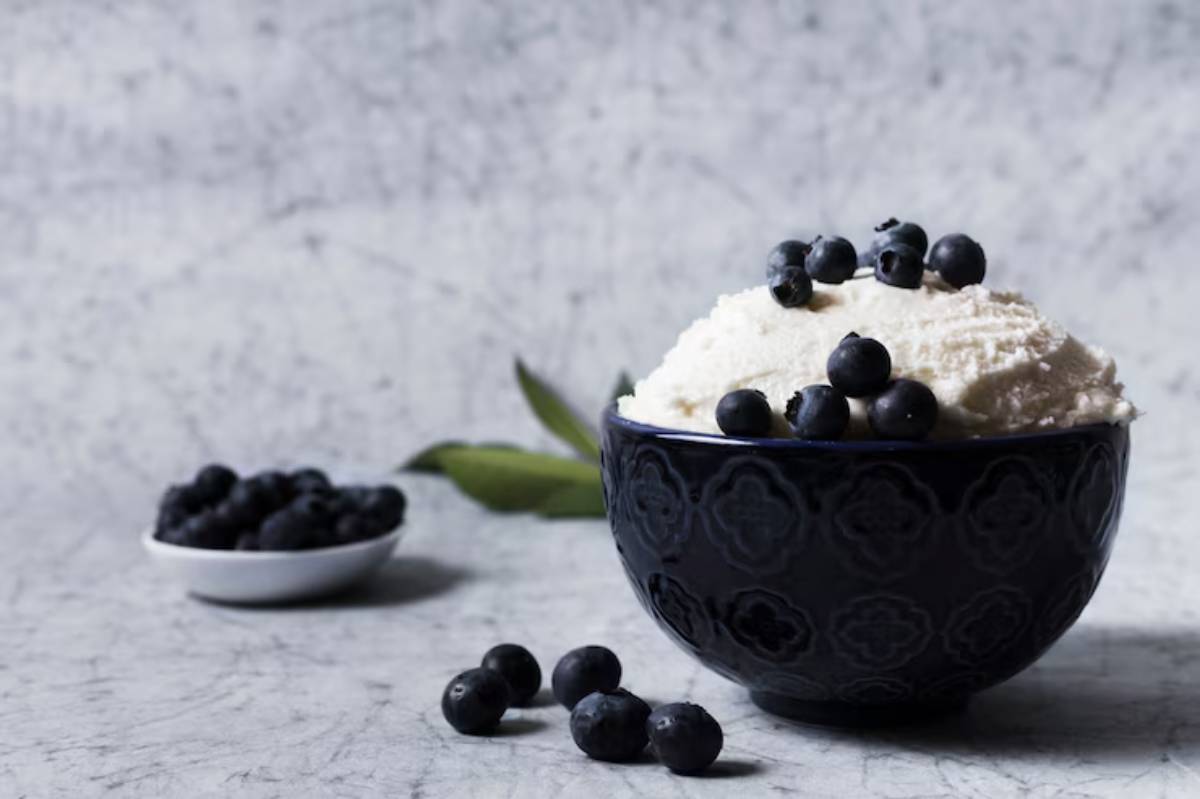 A dark blue bowl filled with creamy white dessert, topped with fresh blueberries, beside a small dish of blueberries.