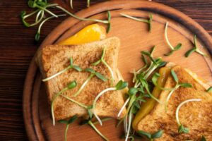 Two golden grilled cheese sandwiches topped with fresh microgreens, served on a round wooden plate.